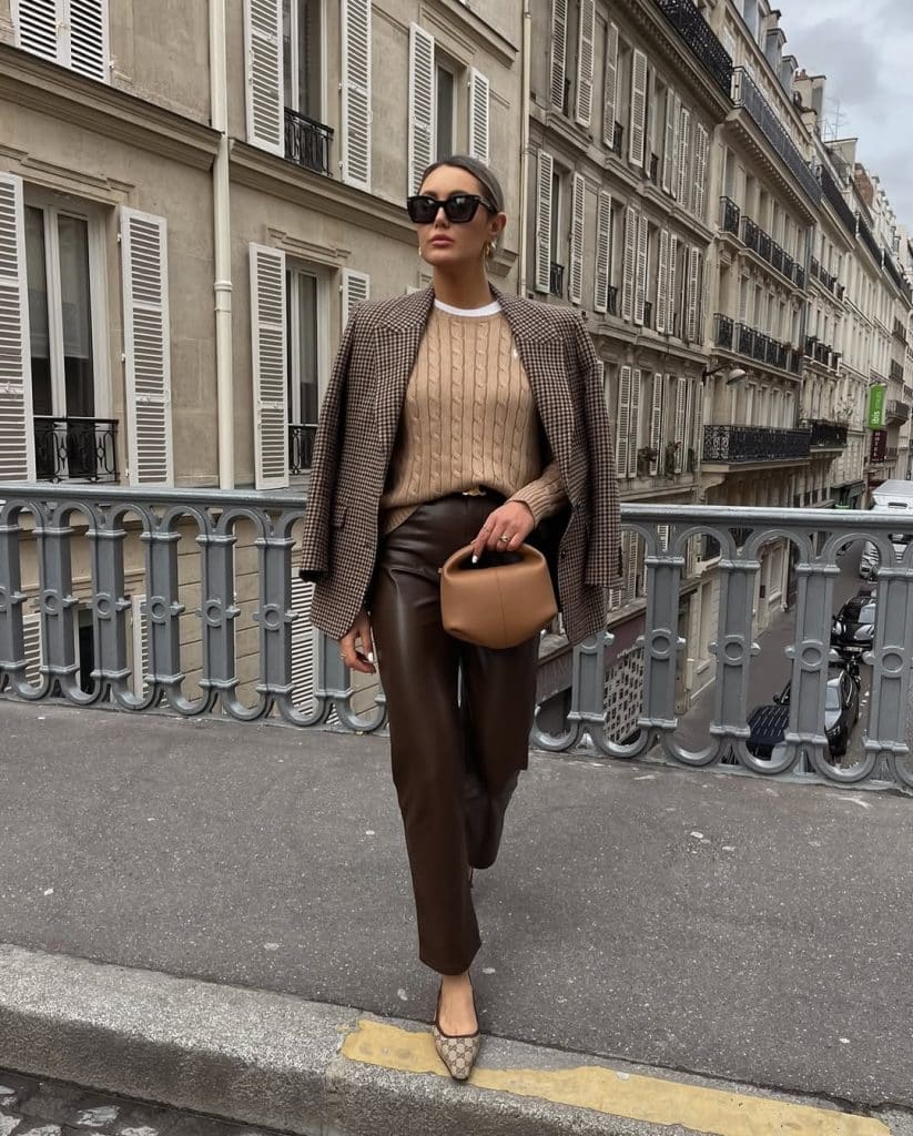 Woman in a plaid blazer and leather trousers walking across a Parisian bridge.