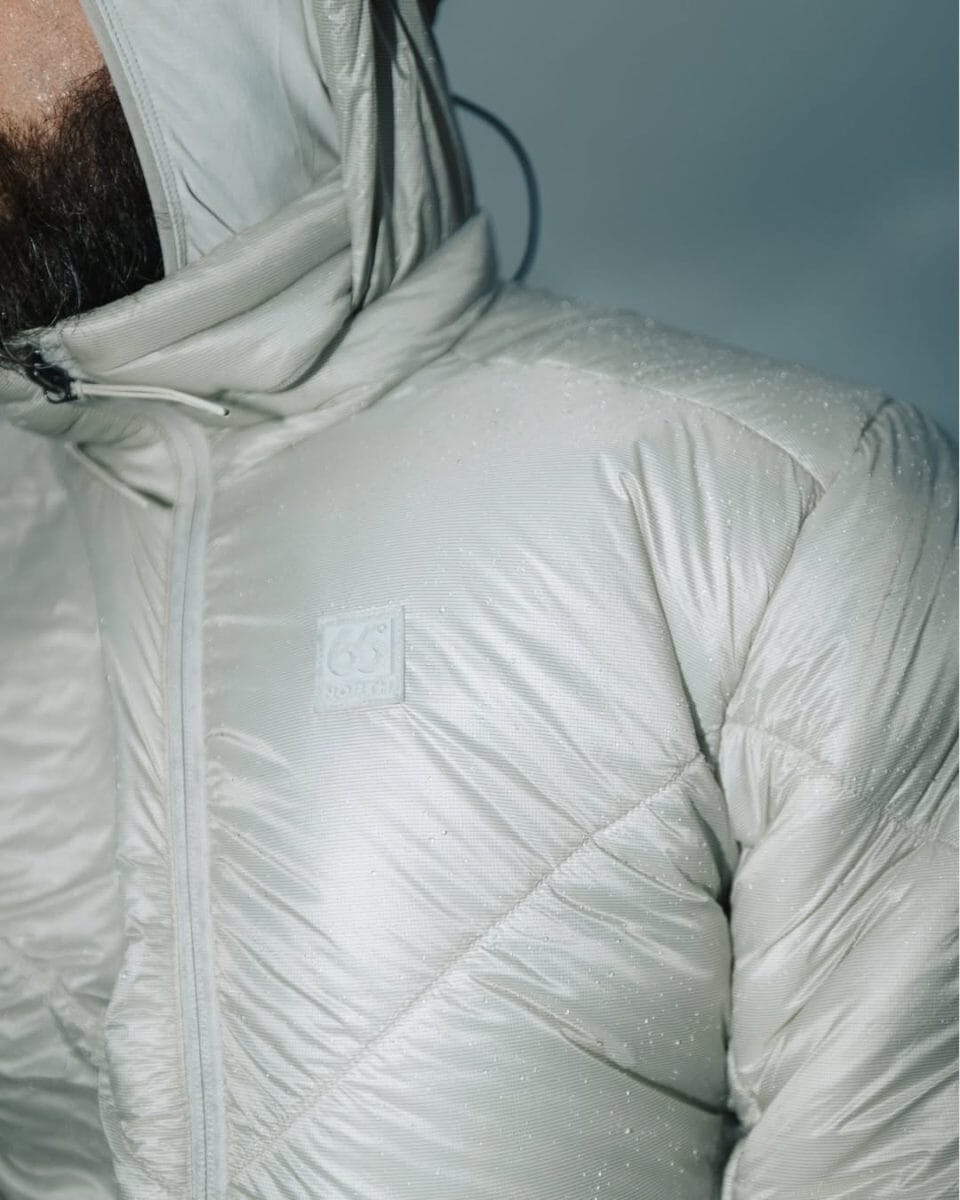 Close-up of a light gray puffer jacket with clear water droplets on the surface.