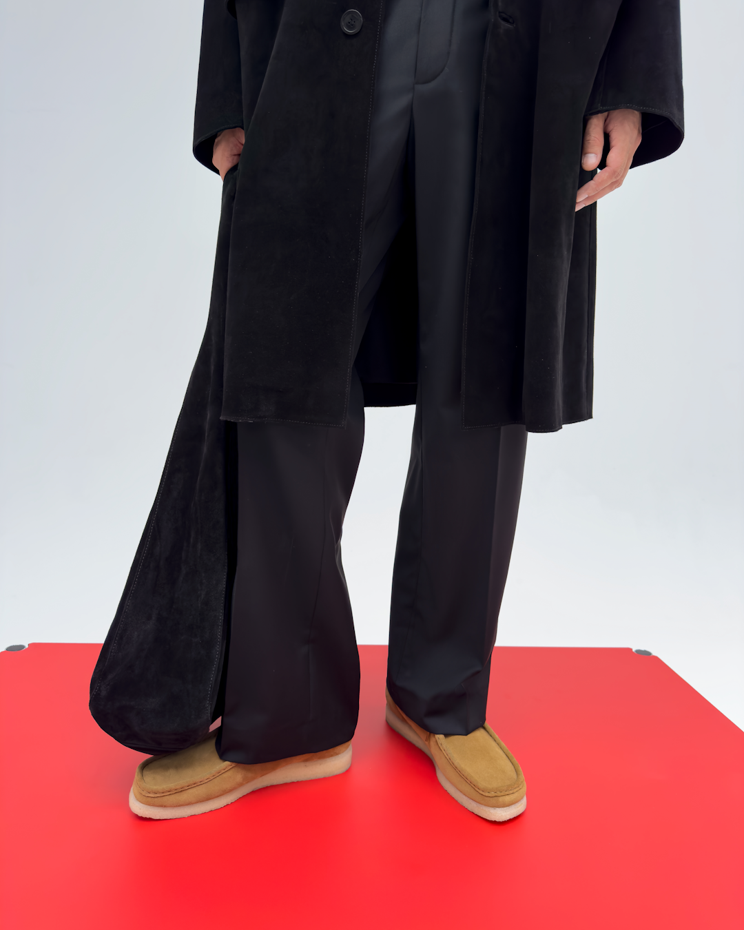 Model wearing a black suede coat and wide-leg trousers with tan loafers.