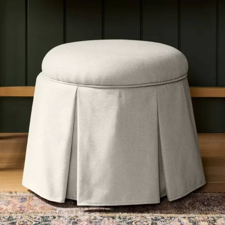 Fabric covered storage ottoman with a box pleat skirt design.