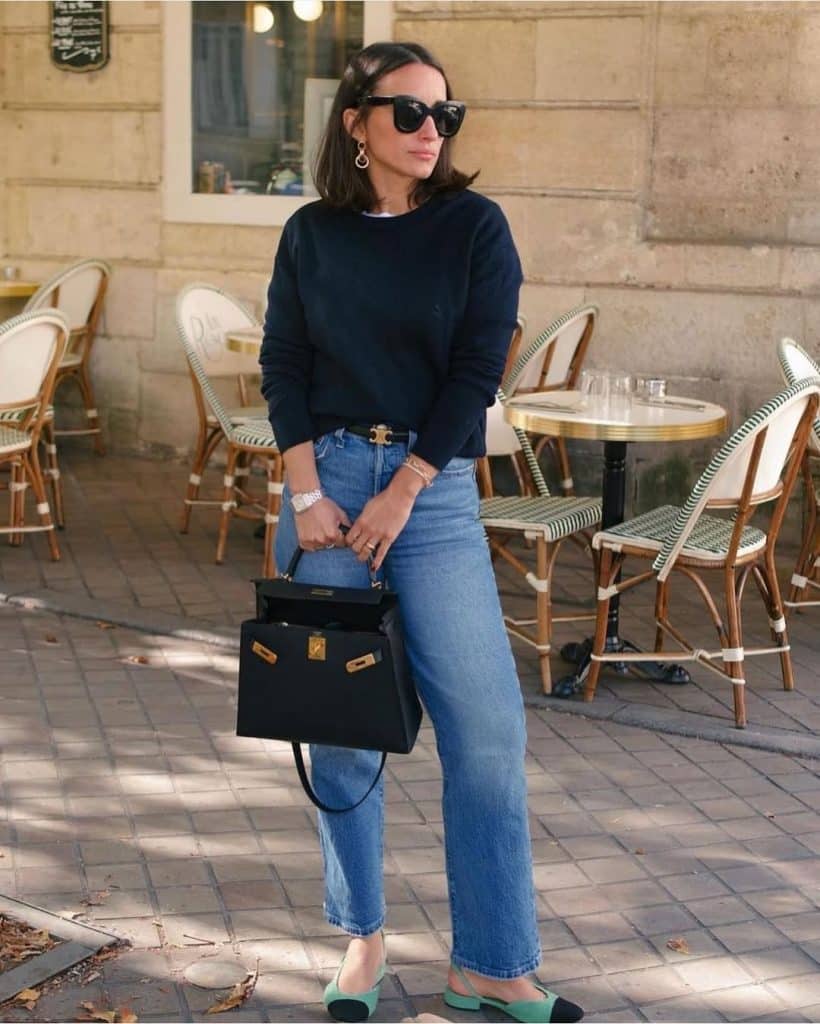 Woman in a navy sweater and wide-leg jeans carrying a luxury black handbag.