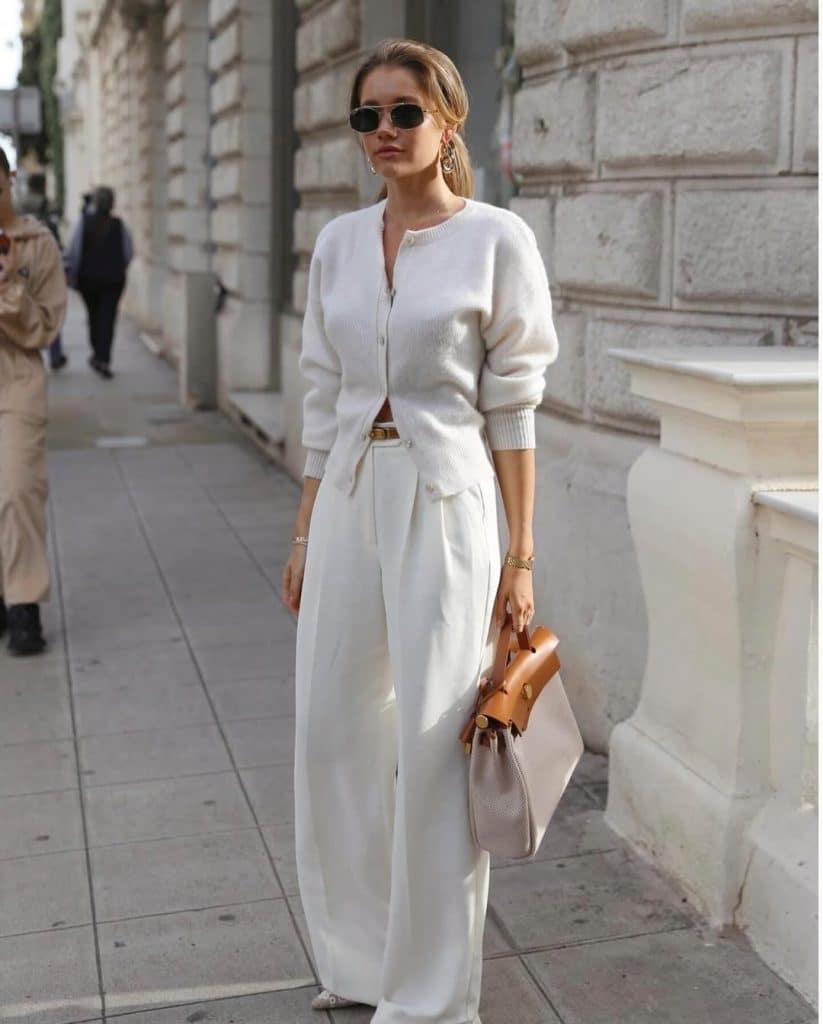 A woman wearing an all-white cardigan and wide-leg trousers outfit walking on a city sidewalk.