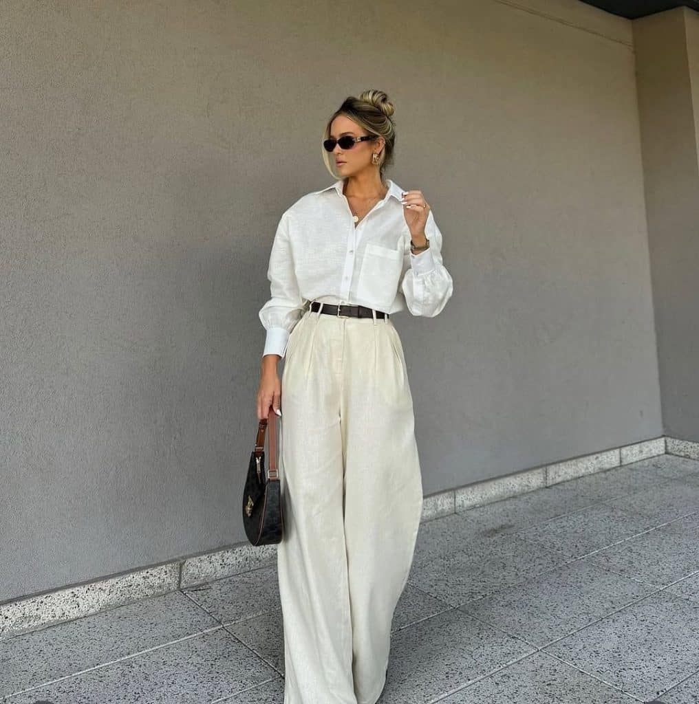 A woman in a minimalist white oversized blouse and cream wide-leg trousers.
