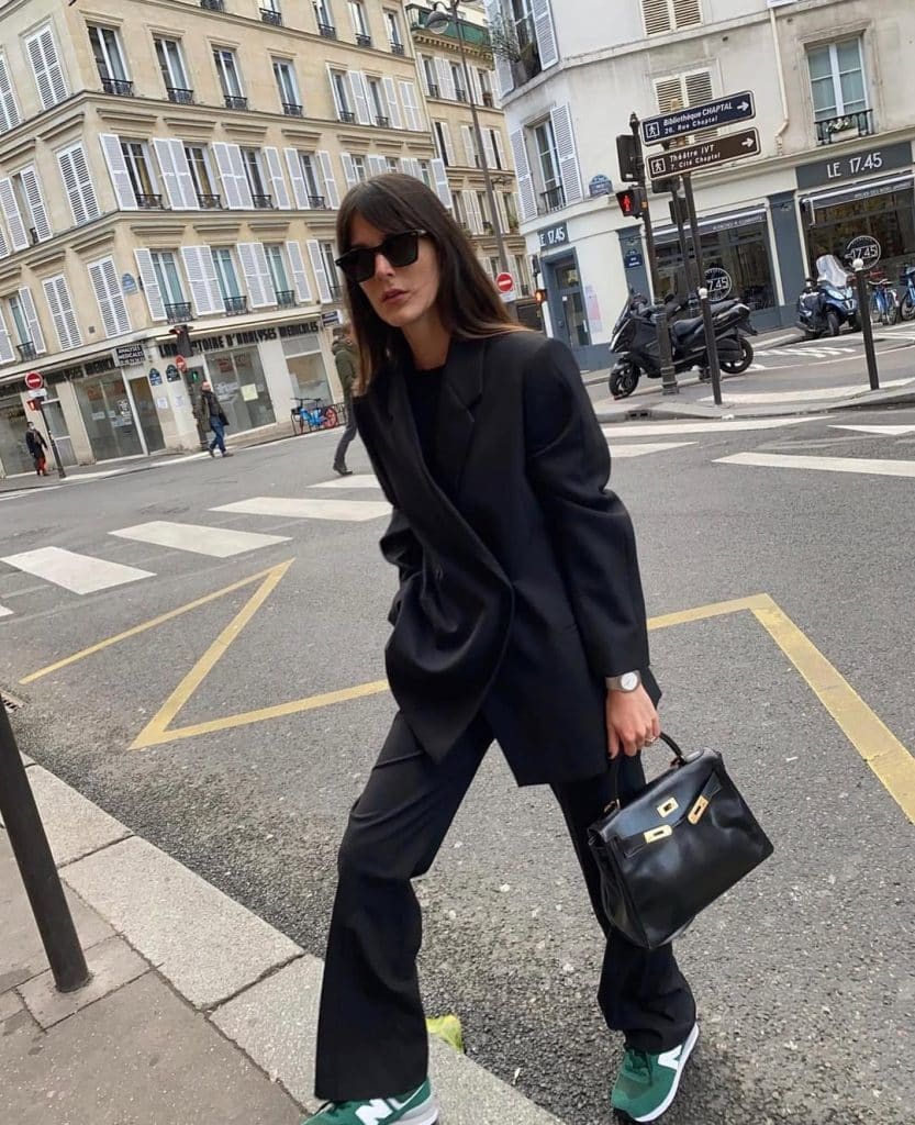 Woman in an oversized black blazer suit and green sneakers crossing a Parisian street.
