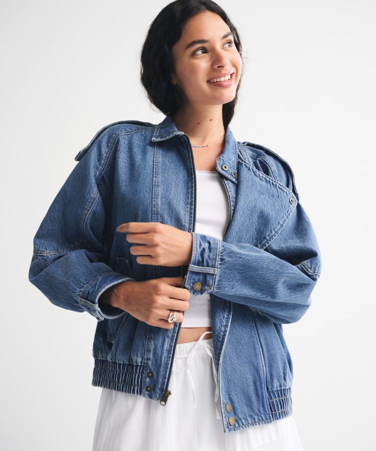 Model wearing a relaxed denim bomber jacket with a faded wash.