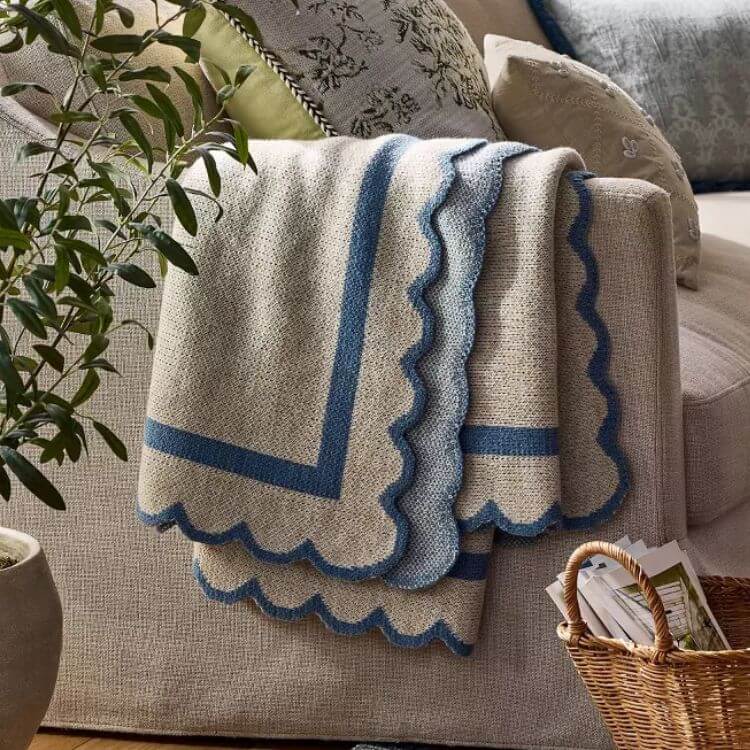 Neutral colored throw blanket with scalloped decorative edges.