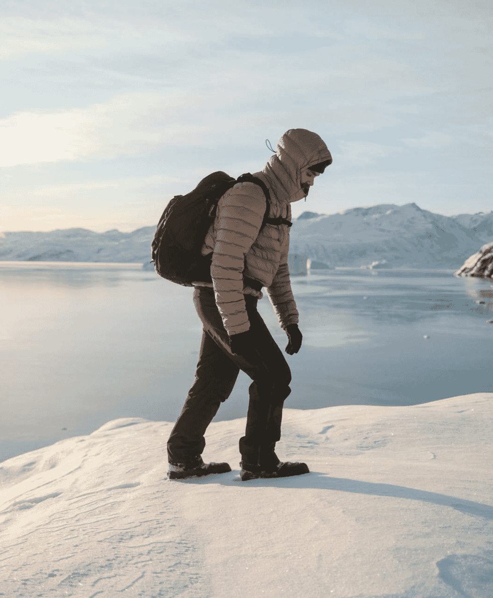 A hiker with a backpack walking across a snowy mountain landscape.