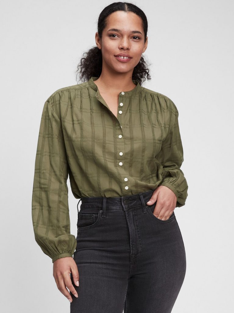 A woman wearing an olive green plaid puff-sleeve blouse and dark denim.