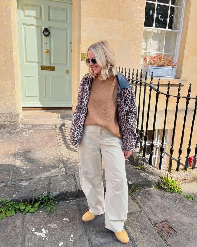 Woman in a leopard-print jacket, wide-leg trousers, and yellow loafers standing in front of a green door.