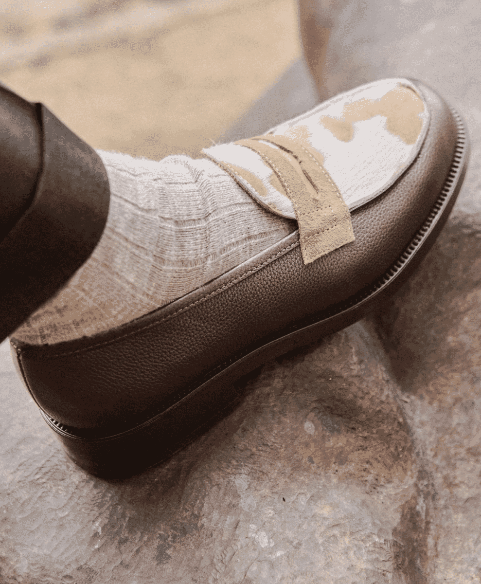 Close-up of a textured brown loafer with ribbed socks on a stone surface.