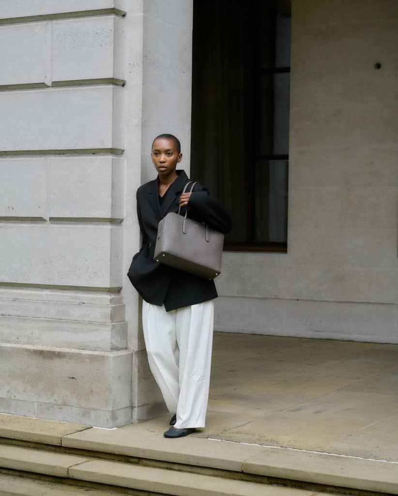 A person with a shaved head in a black oversized blazer and white wide-leg trousers.