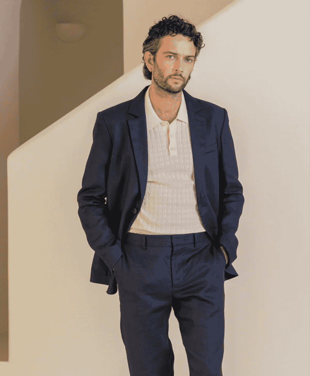 Man with curly hair in a midnight navy blazer over a textured white polo shirt.