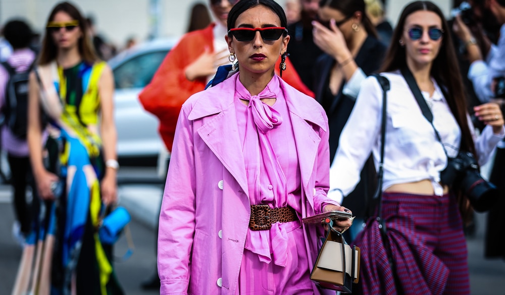 A woman in a bold pink trench coat with a leopard print belt walking through a crowd.