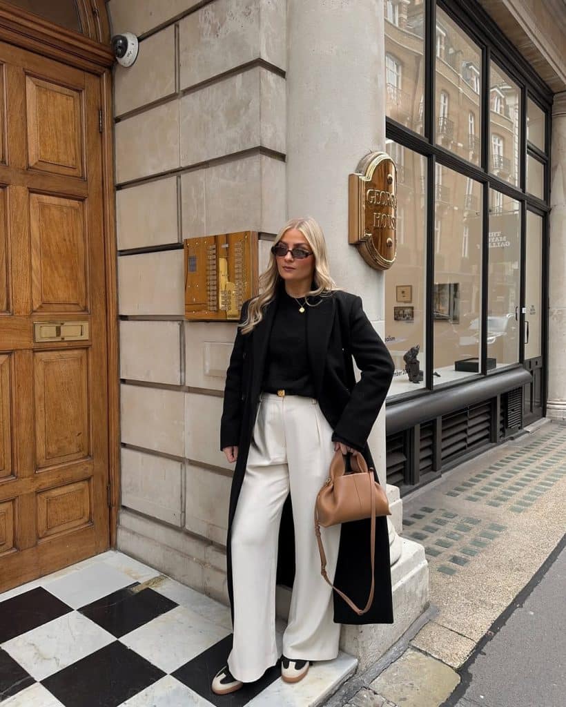Woman in a long black coat and high-waisted white wide-leg trousers.