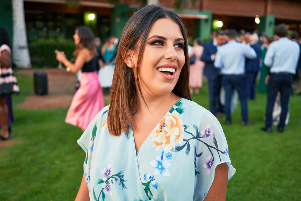 A woman wearing a light blue floral wrap midi dress at an outdoor formal gathering on a lawn.