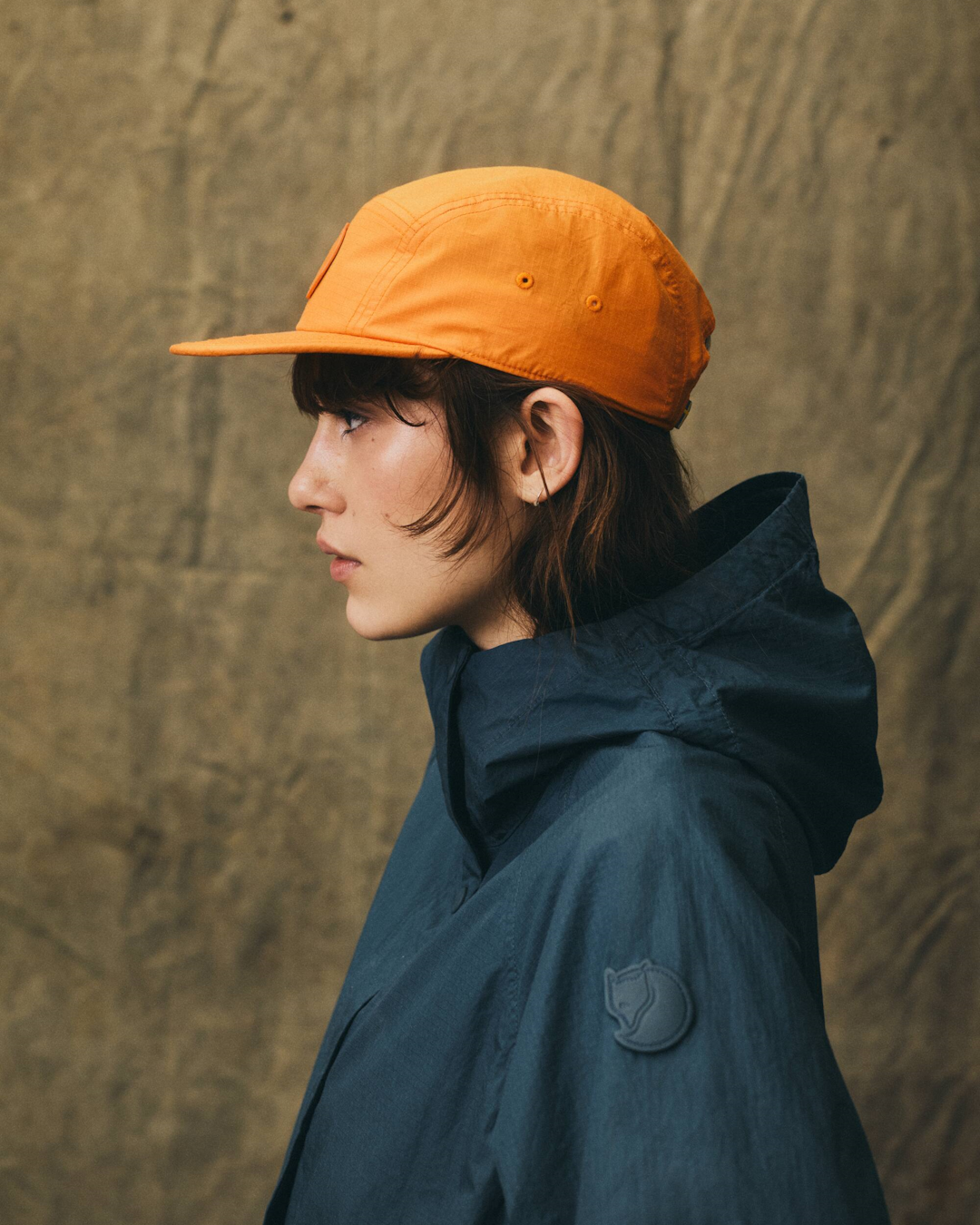 A person wearing the Fjällräven Samlaren hooded jacket with contrasting blue and orange sleeves.