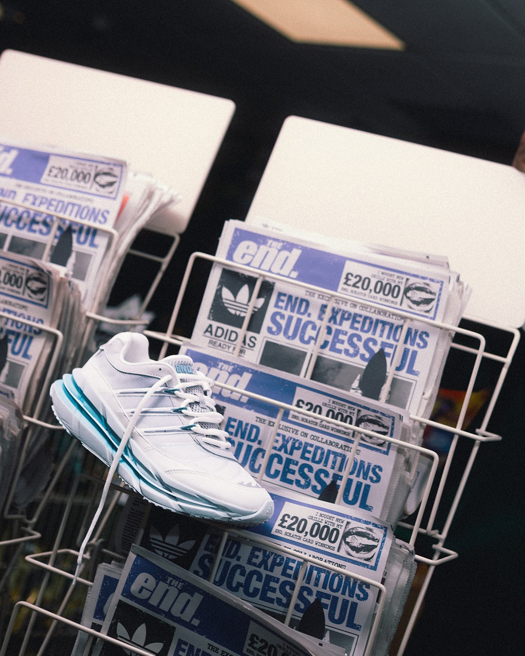 A white adidas sneaker with teal accents displayed on a magazine rack.