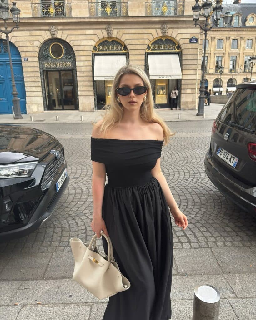 Woman in a black off-the-shoulder midi dress walking in Paris.