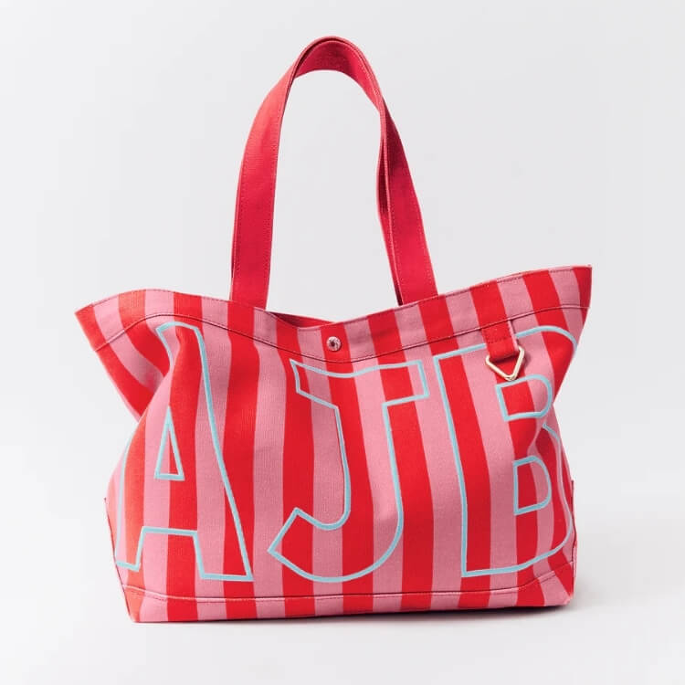 A red and pink striped canvas tote featuring high-contrast AJB monogram lettering.