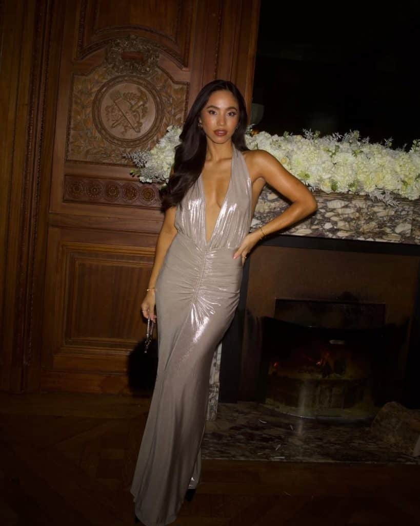 A woman in a shimmering silver halter gown with a deep V-neck in a luxury interior.