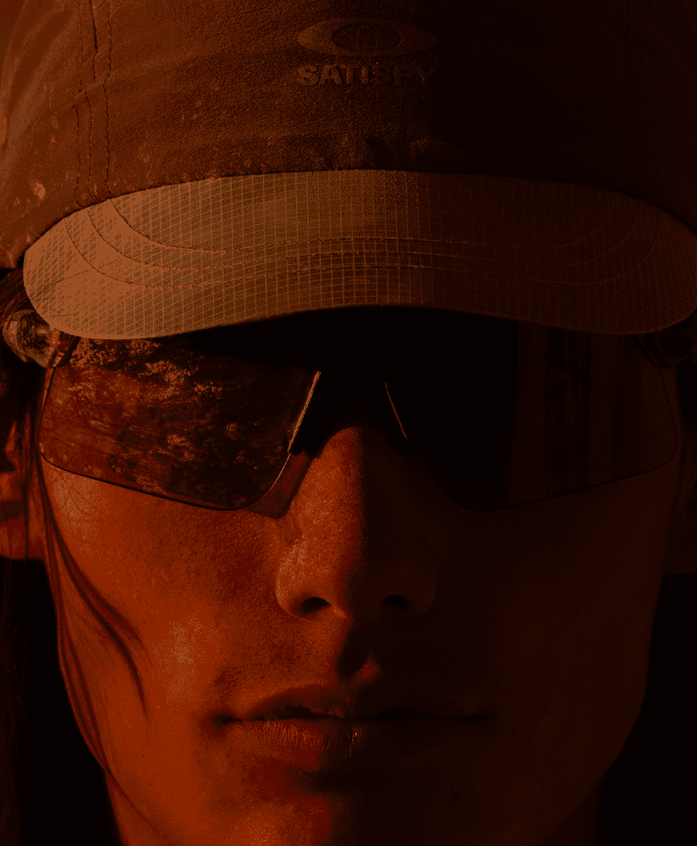 Close-up of a runner wearing a technical cap and Oakley eyewear in a high-contrast orange environment.